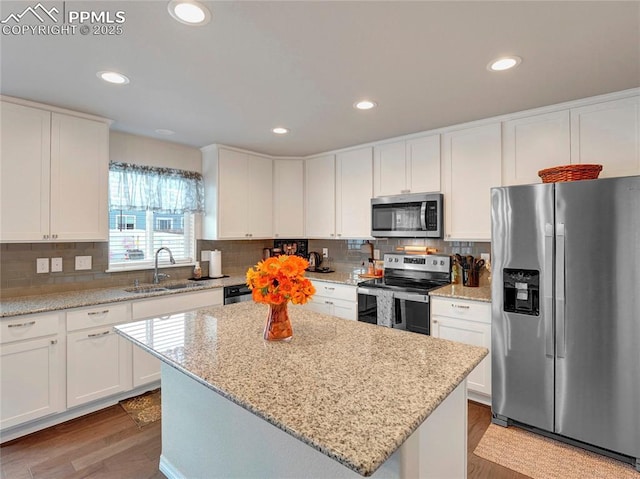 kitchen featuring a sink, a kitchen island, wood finished floors, appliances with stainless steel finishes, and white cabinets