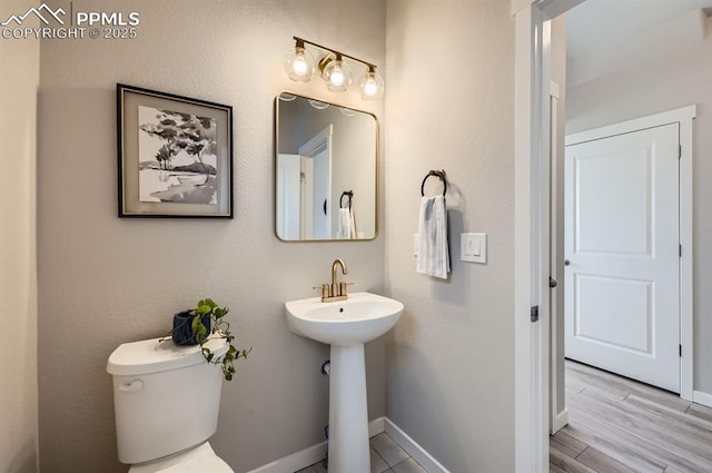 half bath with toilet, wood finished floors, a sink, and baseboards