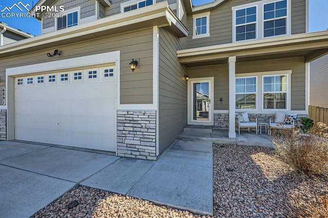view of exterior entry with concrete driveway, a porch, stone siding, and an attached garage