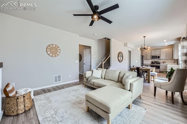 living room with light wood finished floors, visible vents, stairway, and ceiling fan with notable chandelier
