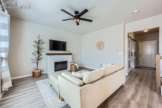 living area with wood finished floors, ceiling fan, baseboards, and a glass covered fireplace