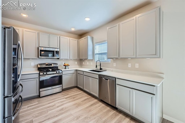 kitchen featuring light wood-style flooring, recessed lighting, appliances with stainless steel finishes, a sink, and gray cabinetry