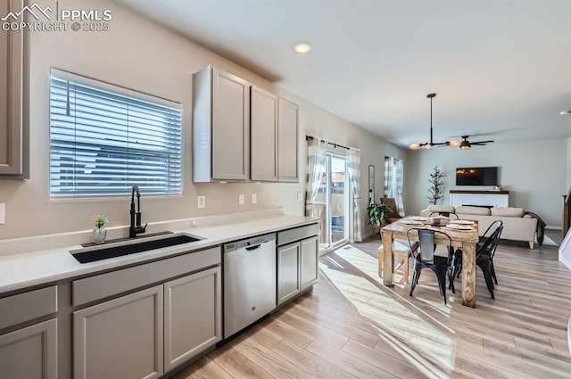 kitchen with a sink, light countertops, light wood-type flooring, gray cabinets, and stainless steel dishwasher
