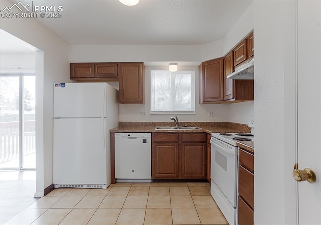 kitchen featuring light tile patterned floors, a sink, dark countertops, white appliances, and under cabinet range hood