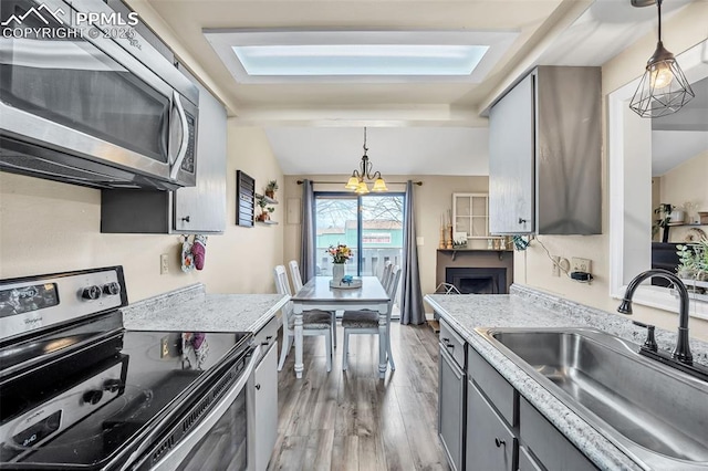 kitchen featuring a sink, light wood-type flooring, pendant lighting, gray cabinets, and appliances with stainless steel finishes