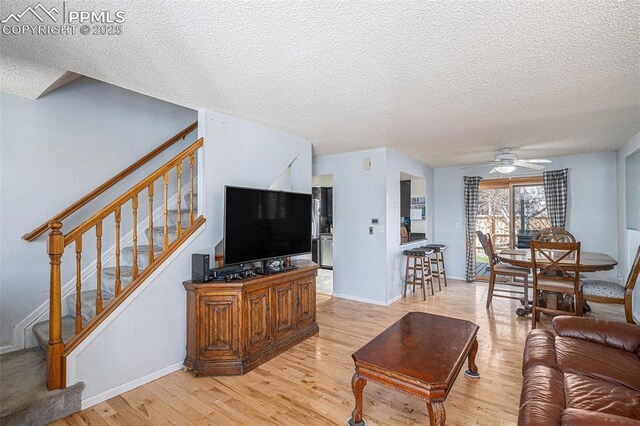 living room with a textured ceiling, light wood-type flooring, baseboards, a ceiling fan, and stairway