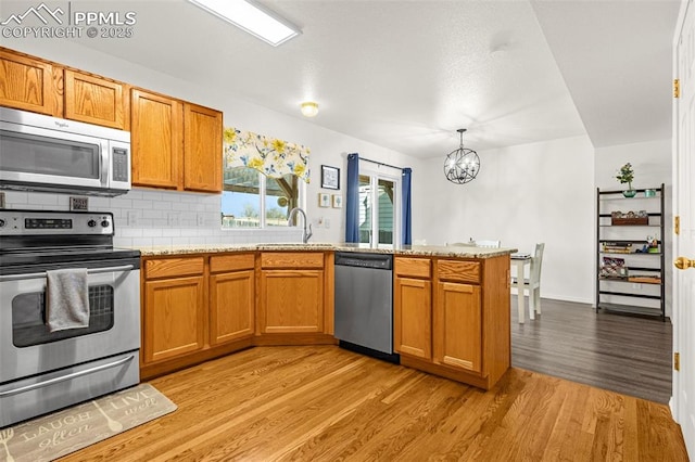 2951 Poughkeepsie Dr, Colorado Springs, CO 80916 - kitchen featuring an inviting chandelier, a peninsula, brown cabinetry, stainless steel appliances, and light wood finished floors