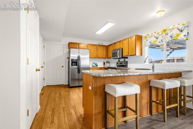 2951 Poughkeepsie Dr, Colorado Springs, CO 80916 - kitchen featuring light wood-type flooring, a peninsula, brown cabinetry, stainless steel appliances, and a sink
