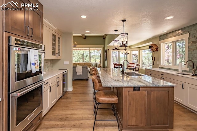 18383 Lazy Summer Way, Monument, CO 80132 - kitchen featuring stainless steel double oven, a sink, wine cooler, light wood-style flooring, and recessed lighting