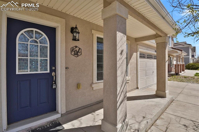 property entrance with a garage, covered porch, concrete driveway, and stucco siding