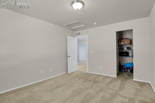 unfurnished bedroom featuring visible vents, baseboards, attic access, a textured ceiling, and carpet flooring