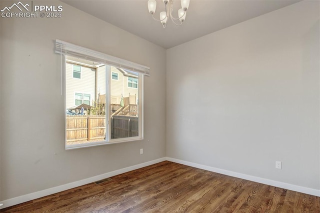 spare room with visible vents, a notable chandelier, dark wood-style floors, and baseboards