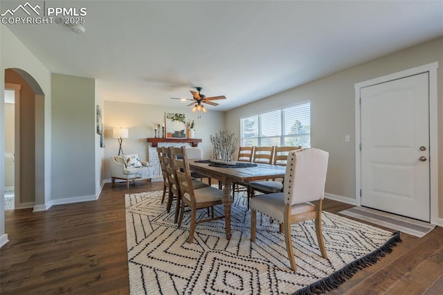 dining room with arched walkways, ceiling fan, baseboards, and dark wood-type flooring