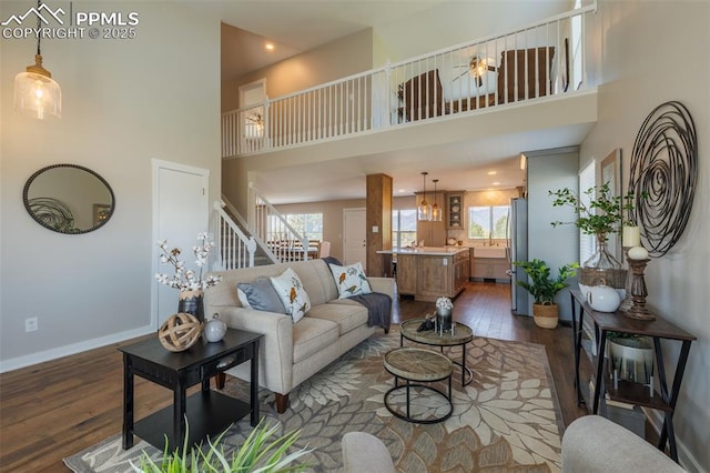 living room with a towering ceiling, dark wood finished floors, stairs, baseboards, and recessed lighting