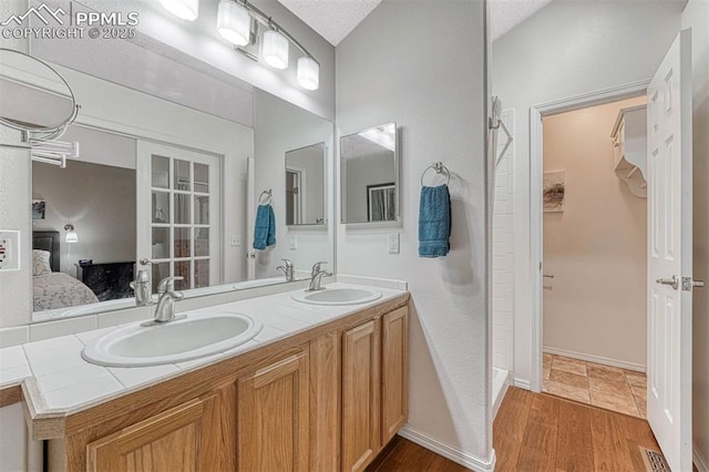 bathroom featuring double vanity, a sink, ensuite bath, and wood finished floors