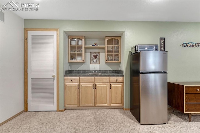 kitchen with dark countertops, light colored carpet, a sink, freestanding refrigerator, and glass insert cabinets