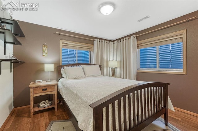 bedroom with baseboards, visible vents, and wood finished floors