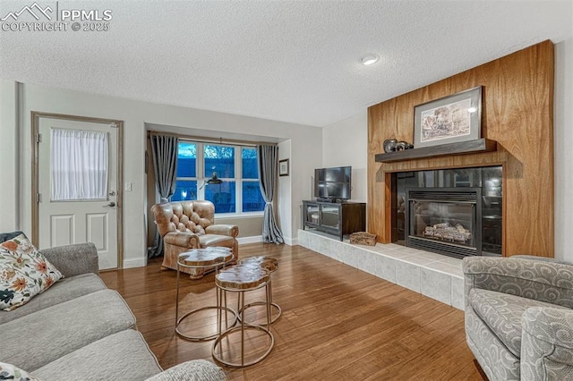 living area with baseboards, a textured ceiling, wood finished floors, and a fireplace