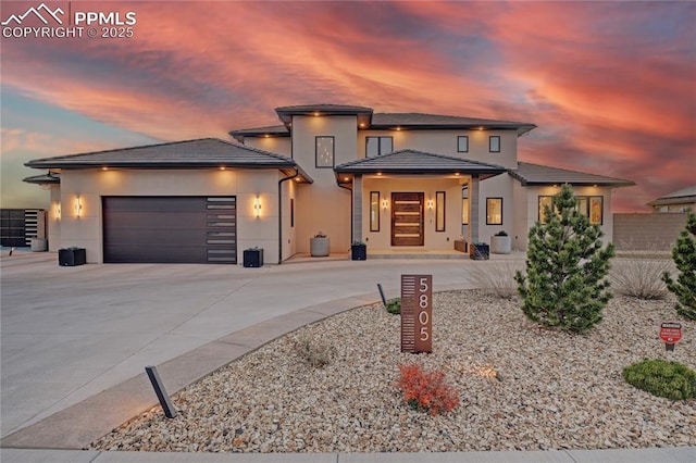 prairie-style home featuring a garage, stucco siding, a tile roof, and concrete driveway