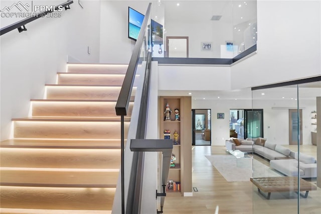 stairs with wood finished floors and a towering ceiling