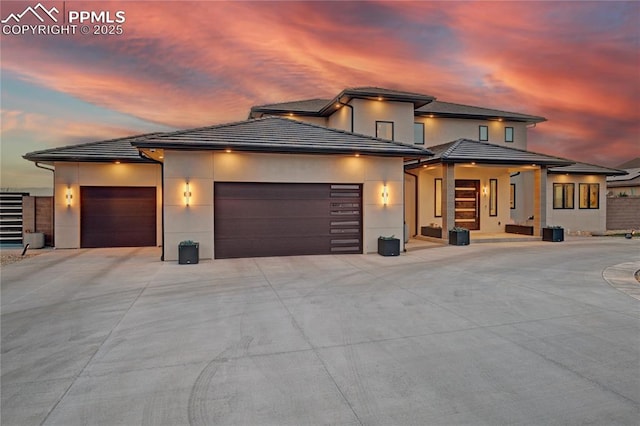 prairie-style home featuring stucco siding, driveway, a tiled roof, and a garage