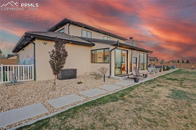 rear view of property featuring a chimney, fence, a patio area, a lawn, and stucco siding