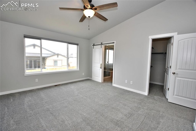 unfurnished bedroom with baseboards, vaulted ceiling, ensuite bathroom, carpet floors, and a walk in closet