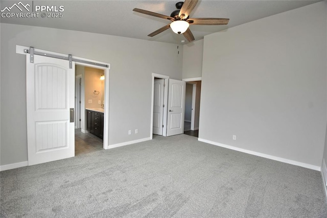 unfurnished bedroom with ensuite bathroom, baseboards, a barn door, carpet, and lofted ceiling