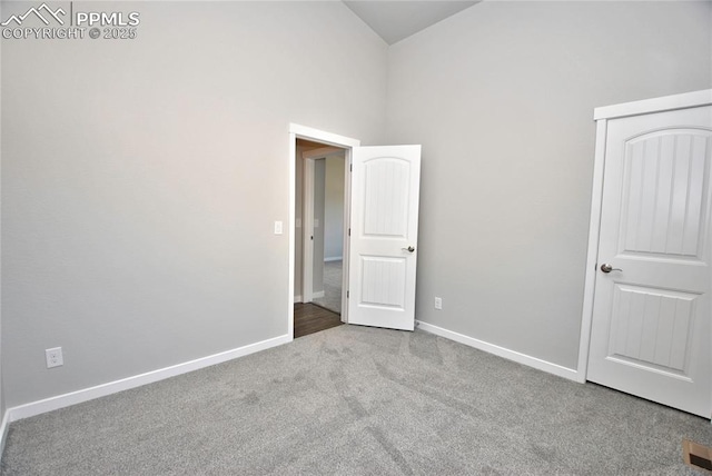 unfurnished bedroom with high vaulted ceiling, carpet flooring, and baseboards