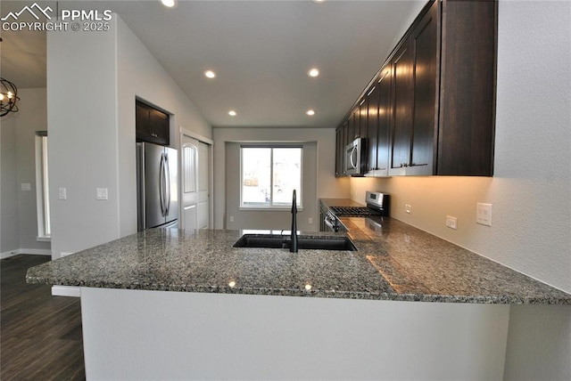 kitchen featuring a peninsula, recessed lighting, dark stone countertops, a sink, and stainless steel appliances