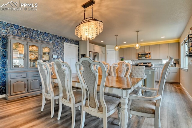 dining room featuring light wood finished floors, a notable chandelier, baseboards, and wallpapered walls