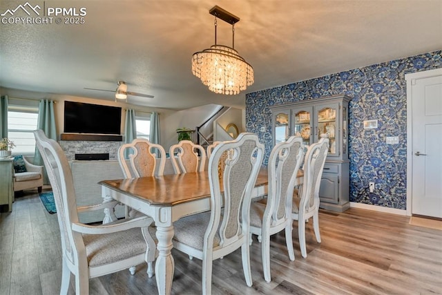 dining area featuring light wood-style flooring, wallpapered walls, ceiling fan with notable chandelier, and baseboards