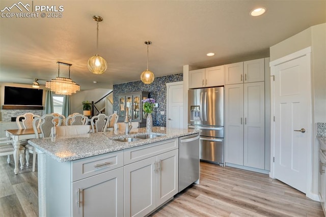 kitchen featuring hanging light fixtures, appliances with stainless steel finishes, an island with sink, light wood finished floors, and wallpapered walls