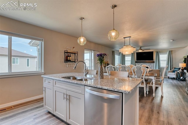 kitchen featuring visible vents, decorative light fixtures, dishwasher, a sink, and light wood-type flooring