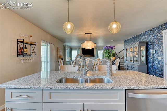 kitchen with light stone countertops, dishwasher, a sink, decorative light fixtures, and wallpapered walls