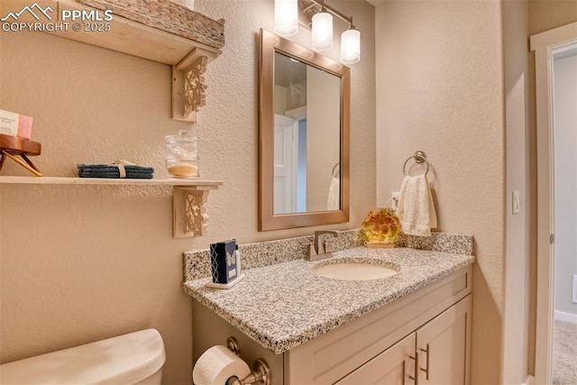 half bathroom featuring toilet, vanity, and a textured wall
