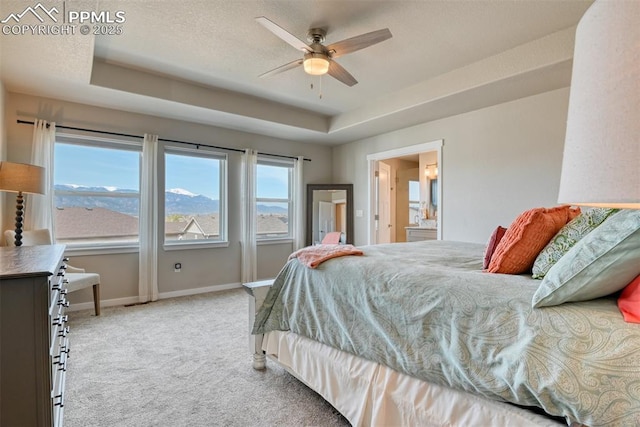 carpeted bedroom featuring a tray ceiling, a textured ceiling, ensuite bathroom, and baseboards