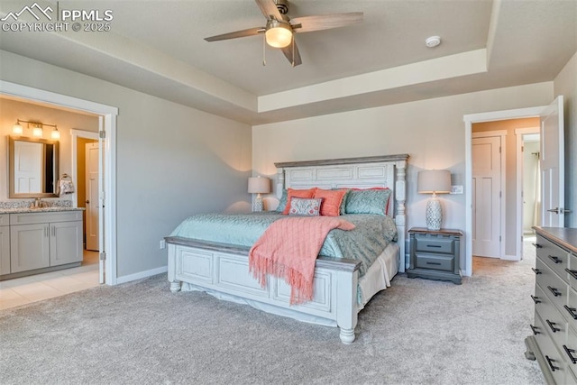 bedroom featuring a tray ceiling, baseboards, ensuite bathroom, and light colored carpet
