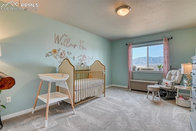 carpeted bedroom with a textured ceiling, a mountain view, baseboards, and a nursery area
