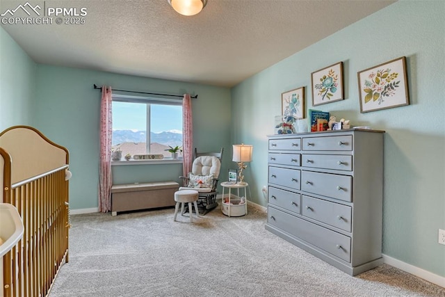 carpeted bedroom featuring a textured ceiling, a mountain view, baseboards, and a nursery area