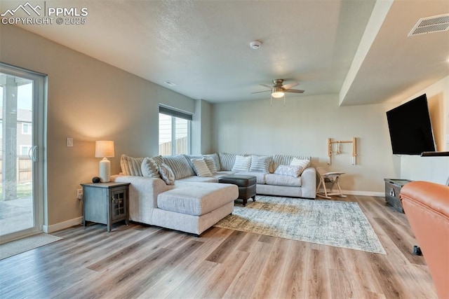 living room featuring visible vents, baseboards, ceiling fan, a wood stove, and light wood-style flooring