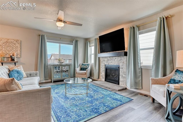 living area featuring ceiling fan, a fireplace, a textured ceiling, visible vents, and wood finished floors