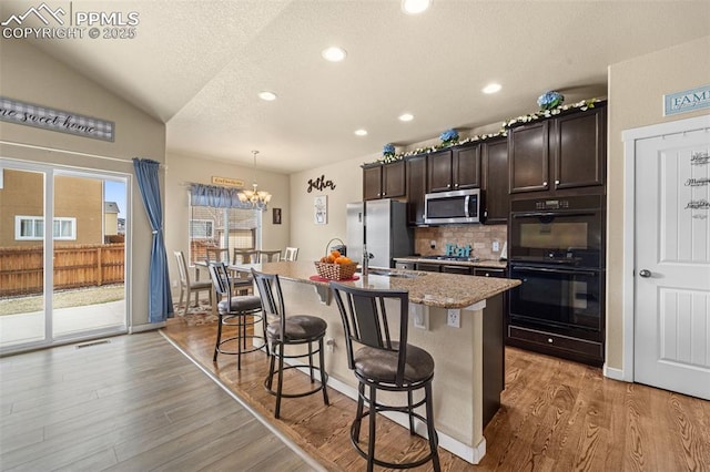 7814 Dry Willow Way, Colorado Springs, CO 80908 - kitchen featuring a kitchen breakfast bar, backsplash, a kitchen island with sink, appliances with stainless steel finishes, and wood finished floors