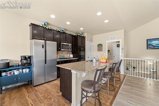 7814 Dry Willow Way, Colorado Springs, CO 80908 - kitchen featuring light wood-type flooring, a kitchen island with sink, a sink, stainless steel appliances, and a breakfast bar area