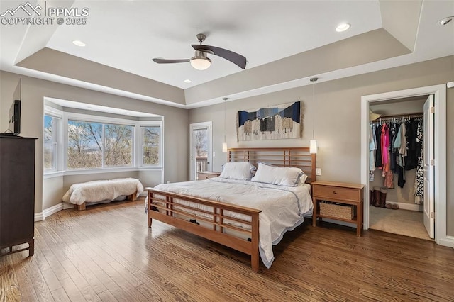 bedroom with a raised ceiling, baseboards, a ceiling fan, wood finished floors, and a walk in closet
