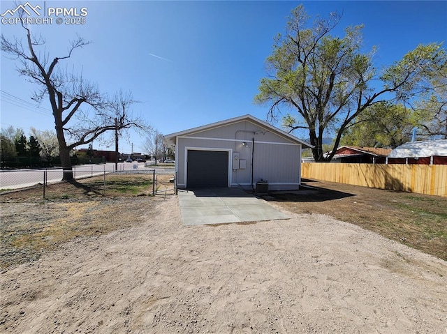 view of outbuilding featuring a garage, driveway, fence, and an outbuilding