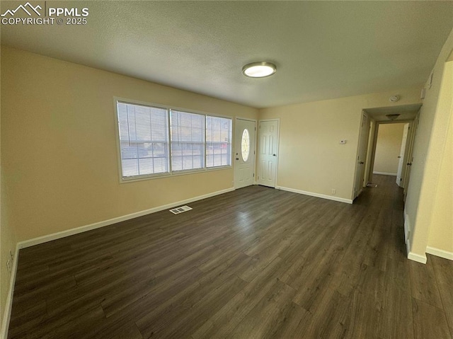 unfurnished room with dark wood-style flooring, visible vents, and baseboards
