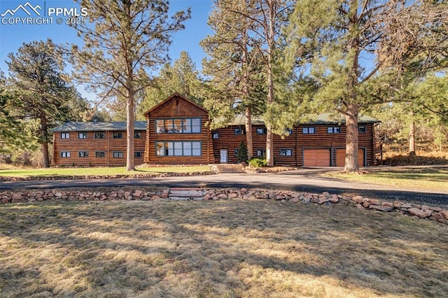 view of front of home with an attached garage, a front lawn, log siding, and aphalt driveway