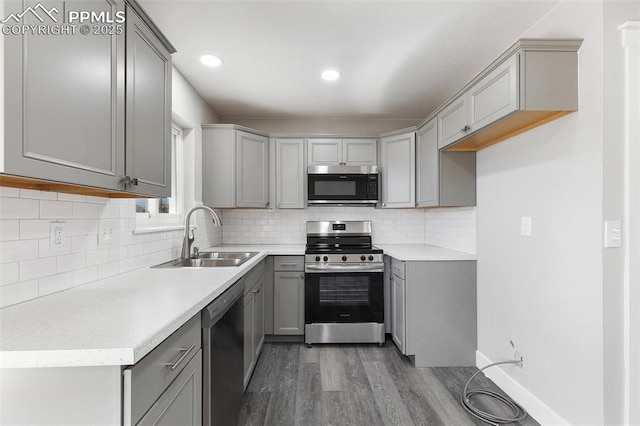 kitchen with a sink, tasteful backsplash, wood finished floors, gray cabinetry, and appliances with stainless steel finishes