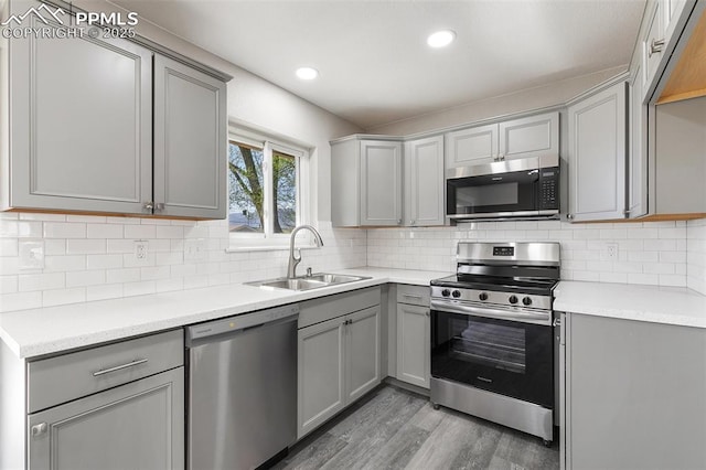 kitchen with a sink, light wood-style flooring, gray cabinets, light countertops, and appliances with stainless steel finishes